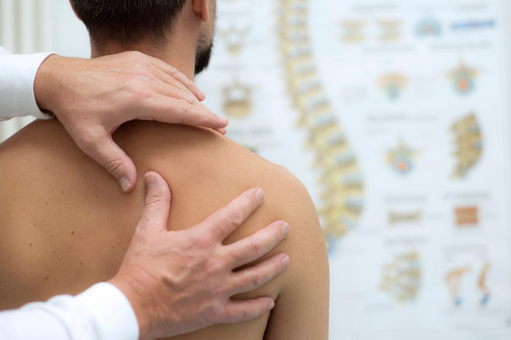 a person sitting down having their shoulder and back examined by a chiropractor