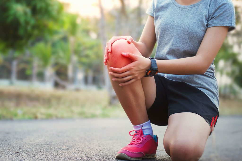 runner is kneeling down holding their painful knee after a sports injury